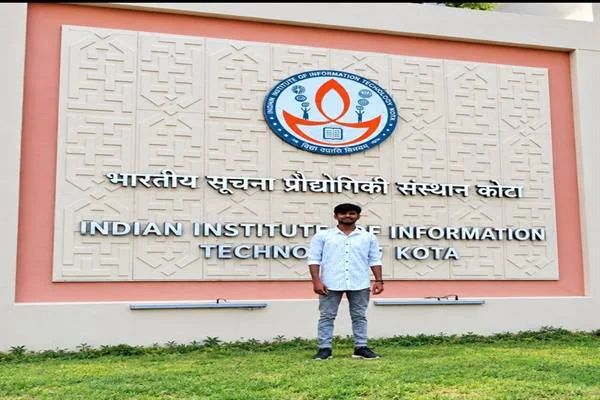 आईआईआईटी कोटा के नाम और प्रतीक चिह्न वाली दीवार के सामने खड़ा एक छात्र